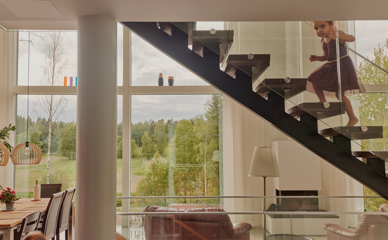 Näkymä talon sisältä ikkunan läpi maalaismaisemaan, lapsi nousee portaita.
