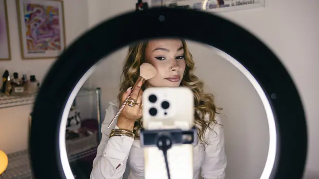 Maria Siivonen levittää poskipunaa kännykän ja rengasvalon edessä.