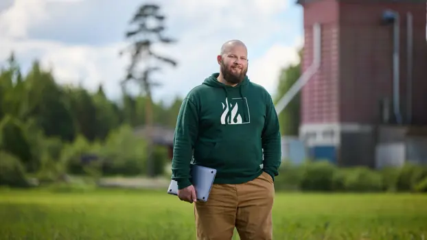 Kasken tilan Reima Välimäki seisoo nurmikolla kannettava tietokone kainalossaan.