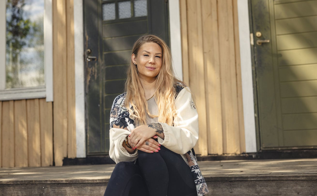 Anette Viima istuu kotitalonsa portailla ja hymyilee.