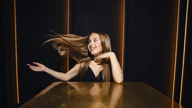 Siiri Virtanen heilauttaa hiuksiaan pöydän ääressä mustalla taustalla ja hymyilee.