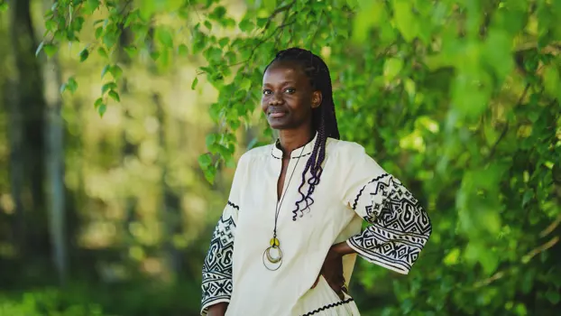 Quivine Ndomo seisoo ulkona valkoisessa asussa, taustalla näkyy puiden lehtiä.