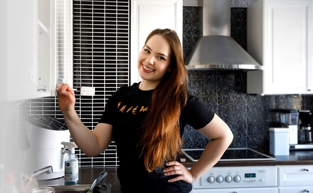 Rosanna Kujala pitää kiinni vaalean keittiön kaapinovesta ja hymyilee.
