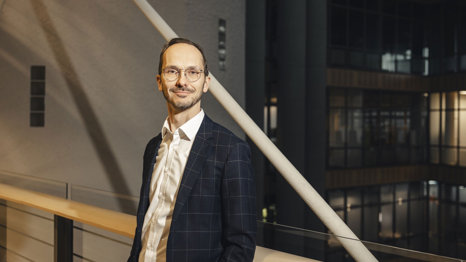 Harri Malinen seisoo puvuntakki päällä yrityksen siltakäytävällä ja hymyilee.