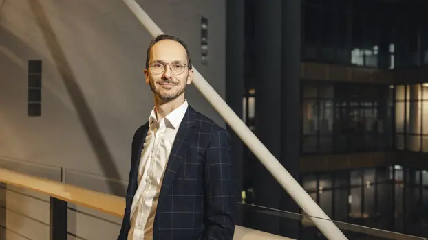 Harri Malinen seisoo puvuntakki päällä yrityksen siltakäytävällä ja hymyilee.