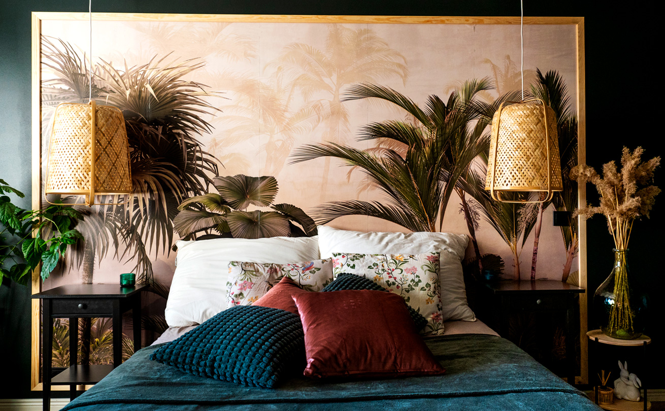 Kuvassa tummanvihreällä päiväpeitolla peitetty sänky, samanvärinen seinä ja palmukuvioisesta tapetista tehty sängynpääty.