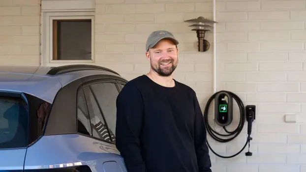 Teemu Pelttari seisoo autonsa edessä ja hymyilee.