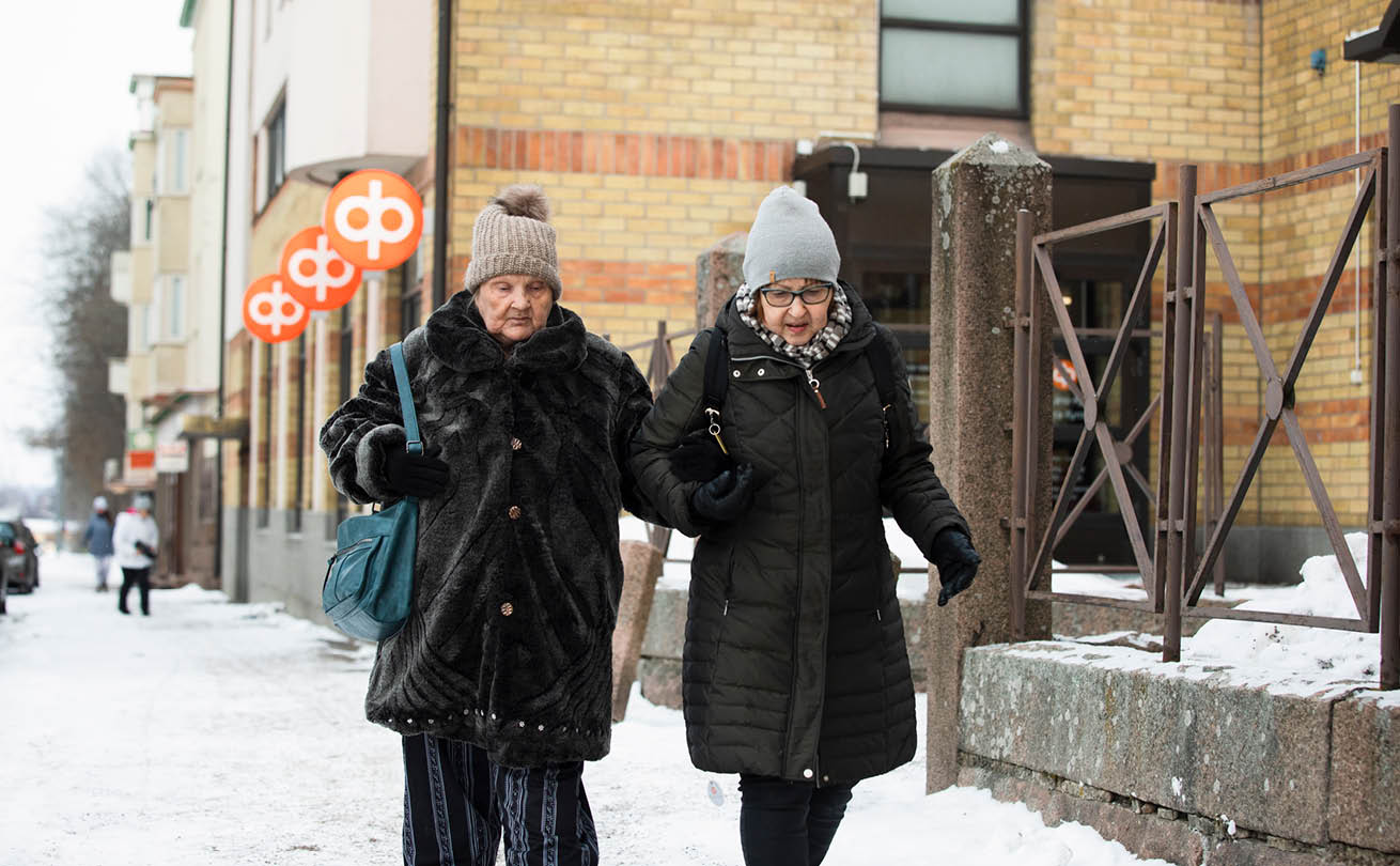 Kaksi naista kulkee käsikynkkää katua pitkin mustissa talvivaatteissa.