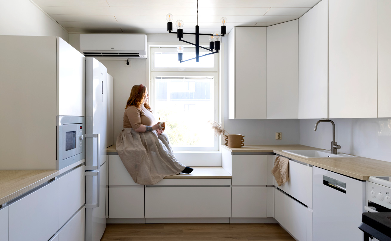 Riina Heinonen istuu keittiössä ikkunan edessä olevalla korokkeella.