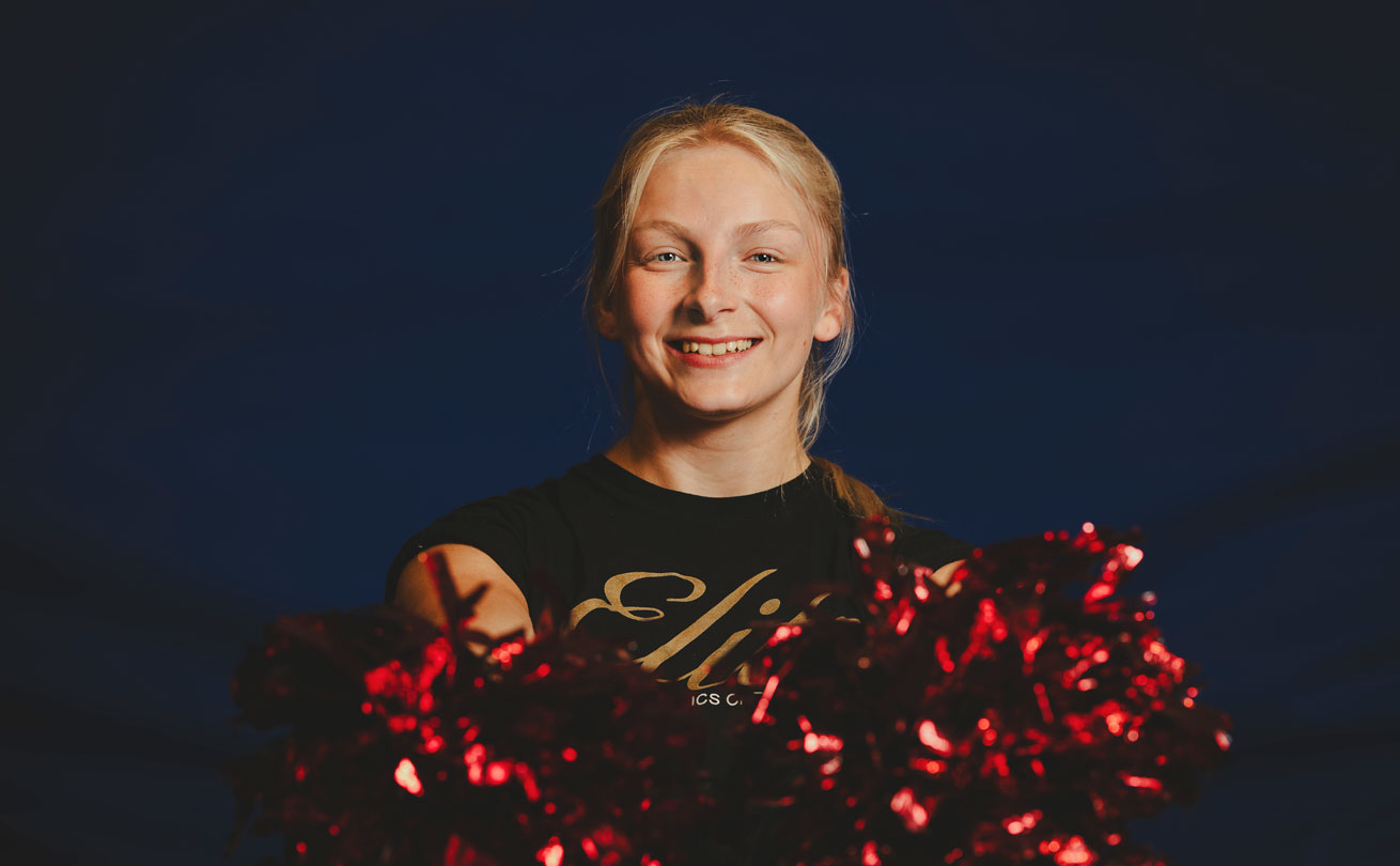 Lähikuva hymyilevästä Ronja Nyholmista punaiset cheerleaderin huiskat kädessä.