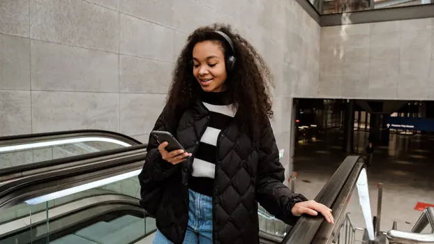 Nuori nainen katsoo puhelinta liukuportaissa.