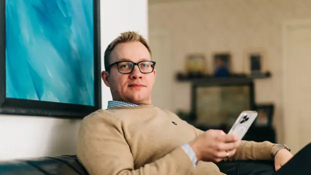 Tuukka Perälä istuu sohvalla kännykkä kädessä ja katsoo suoraan kuvaajaan.