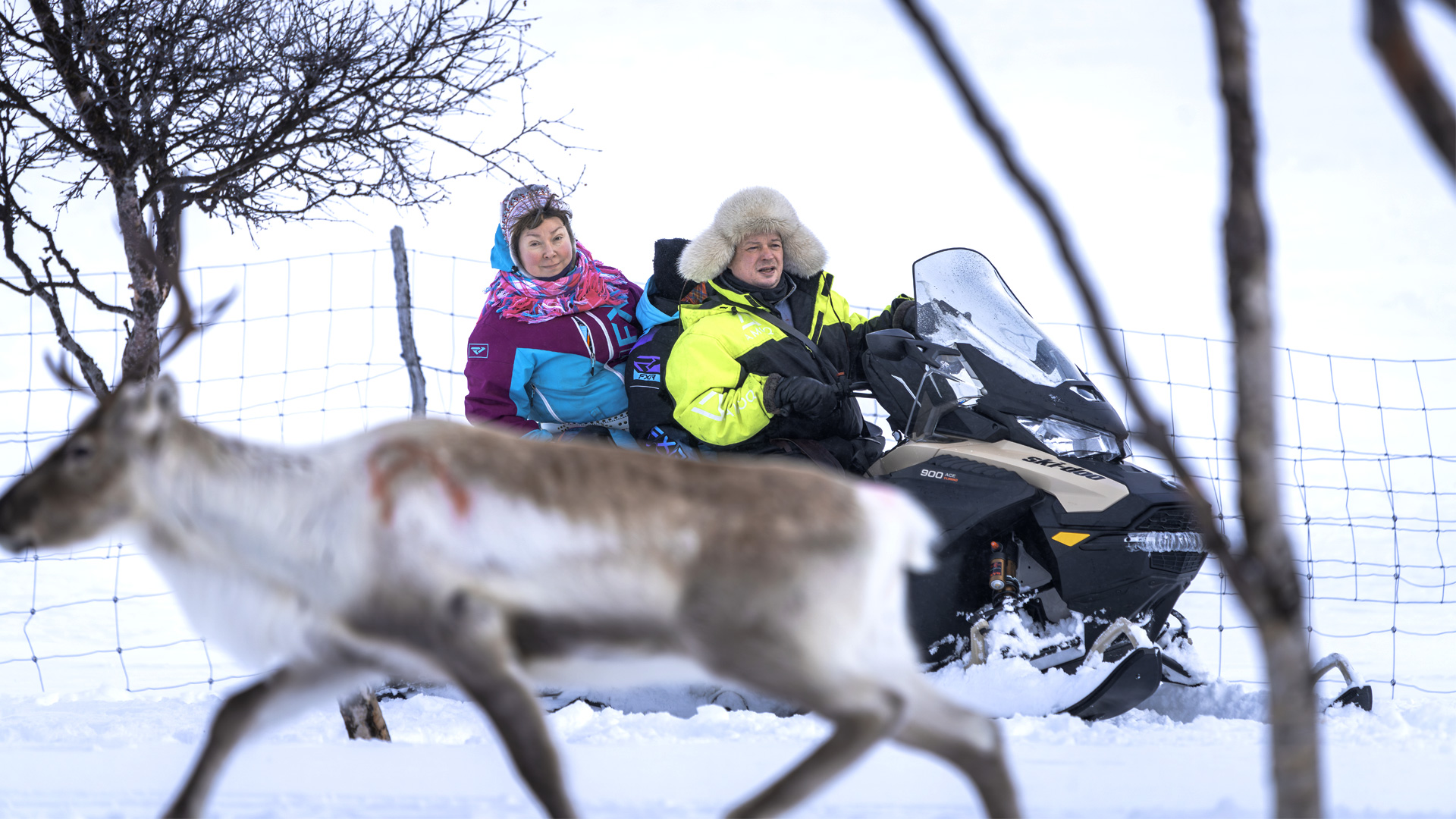 Kuvassa mies, nainen ja lapsi moottorikelkan päällä.