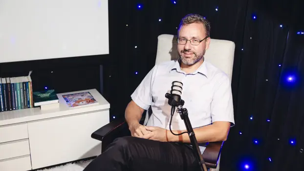 Sven-Erik Holmström istuu tuolissa mikrofonin ääressä ja hymyilee.