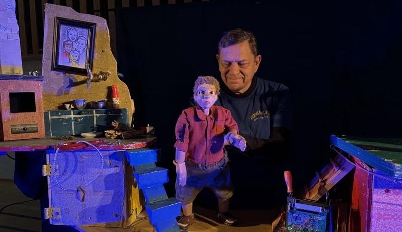 Nukkemestari Hannu Räisä katsoo omatekemäänsä puista nukkea Poika ja korppi -esityksen lavasteissa.