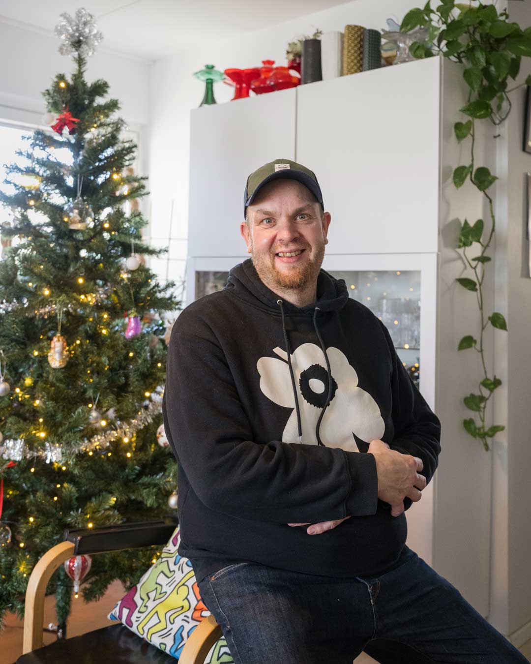 Pekka Laukkanen istuu tuolin käsinojalla joulukuusen edessä ja hymyilee.