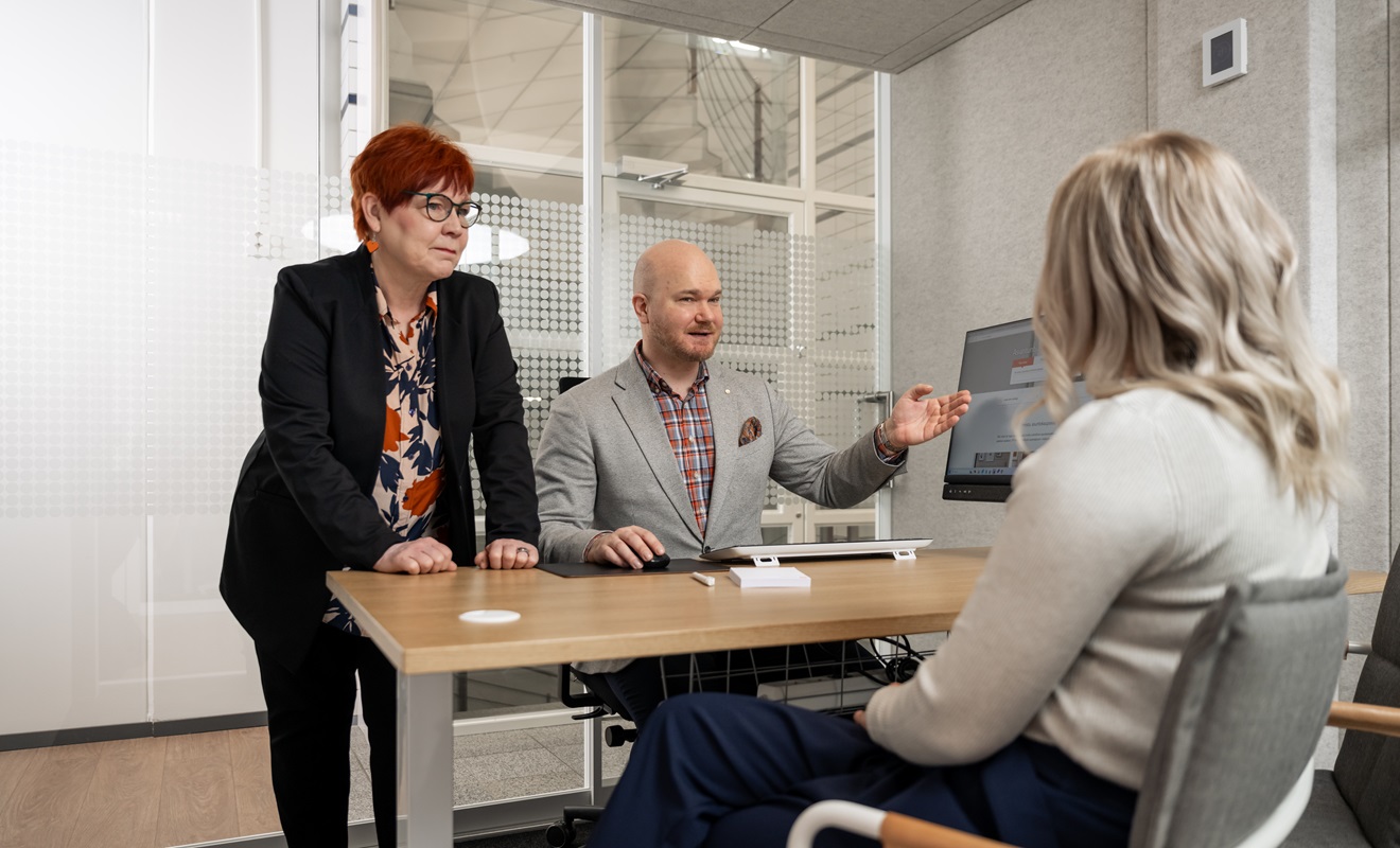 Asiakas ja kaksi pankin asiantuntijaa keskustelevat rahoitusratkaisuista neuvotteluhuoneessa.