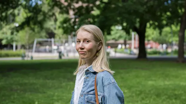Mari Waegelin katsoo kameraan, taustalla näkyy vehreä nurmi ja leikkipuisto puiden katveessa.