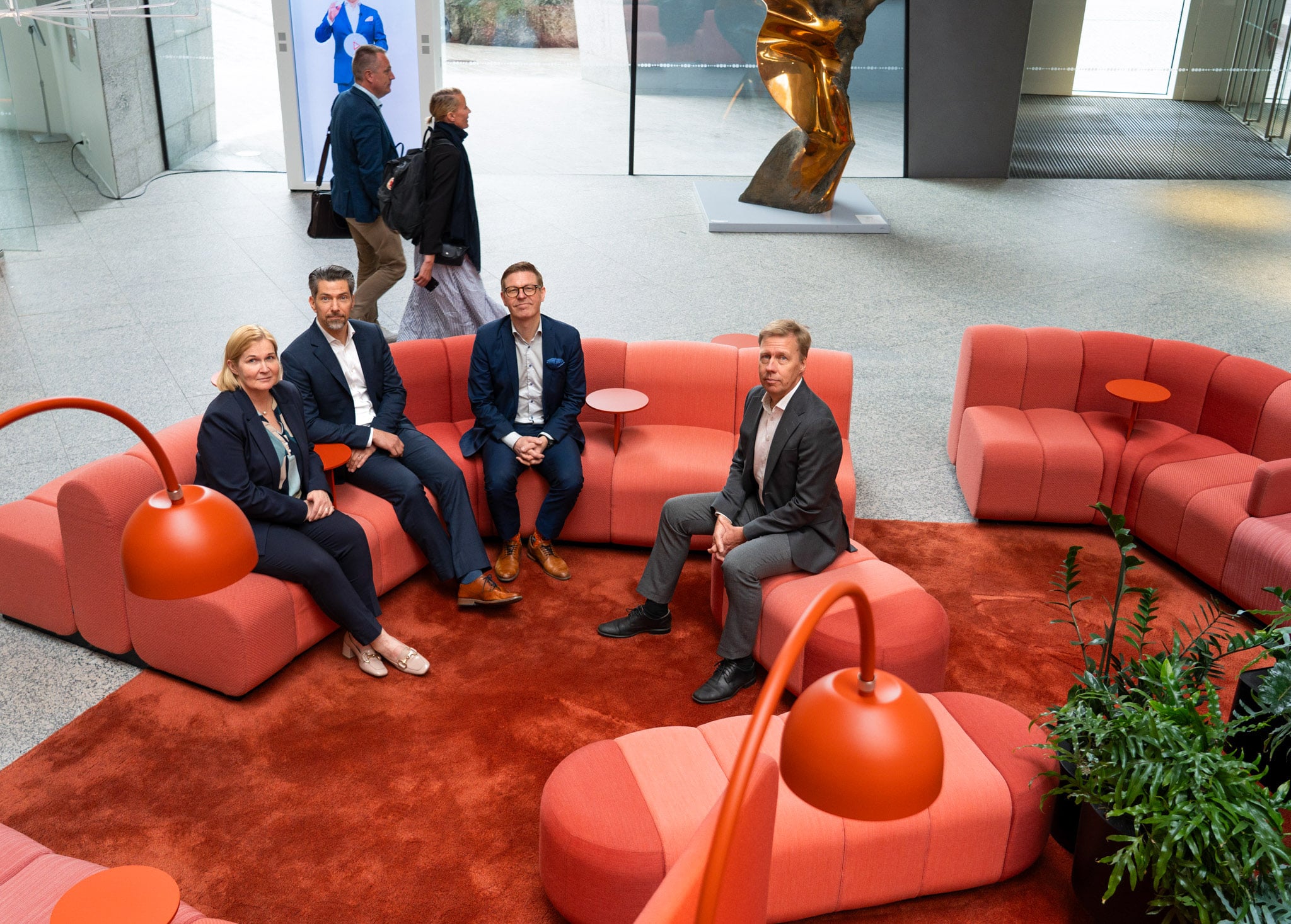 Marika Toikka, Tuomas Haapakoski, Antti Niemelä ja Jussi Haarasilta OP Pohjolan Vallilan konttorin aulassa oransseilla sohvilla.