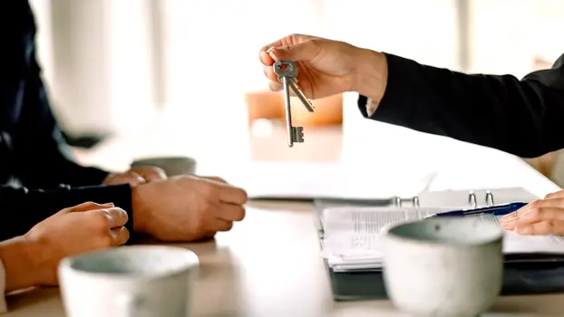 Henkilö antaa kodin avaimia asunnon ostajille pöydän ääressä