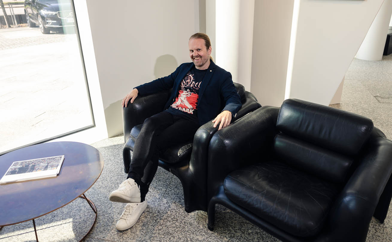 Ville Pekkala istuu sohvalla OP-ryhmän aulassa. Hän katsoo viistosti ylöspäin kohti kuvaajaa ja hymyilee iloisesti.