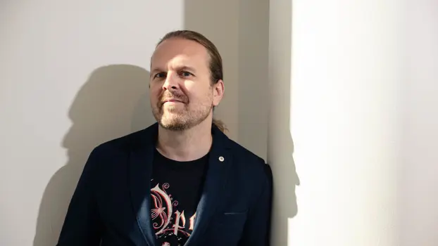 Salkunhoitaja Ville Pekkala pikkutakki päällä, takin alta pilkottaa logollinen t-paita.